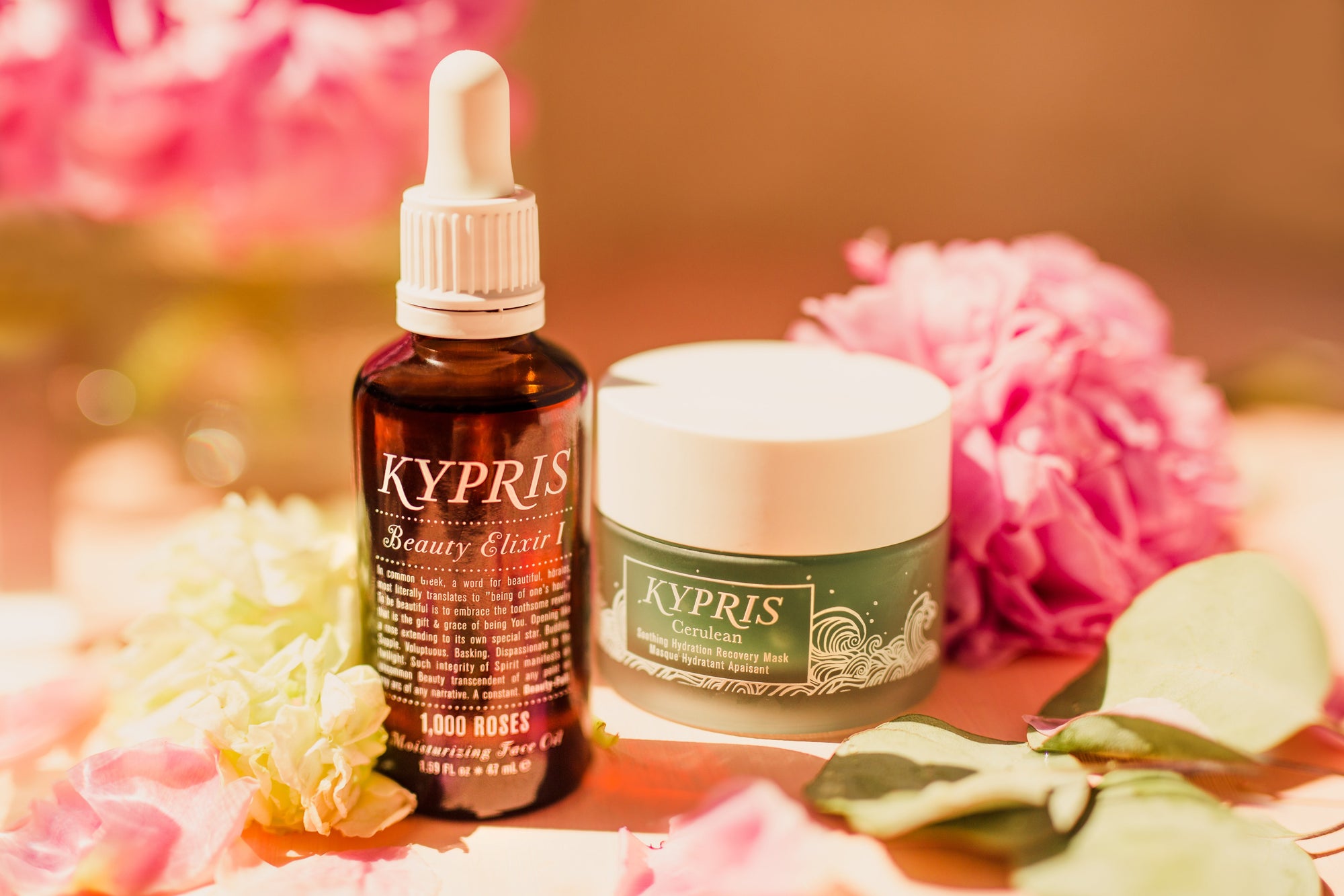 Beauty Elixir I: 1,000 Roses in amber glass bottle sits atop 12.5mL Cerulean mask in clear glass jar showing cerulean blue product color.