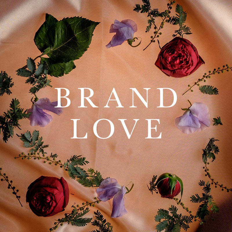 BRAND LOVE surrounded by red roses, purple flowers, and green leaves on soft fabric
