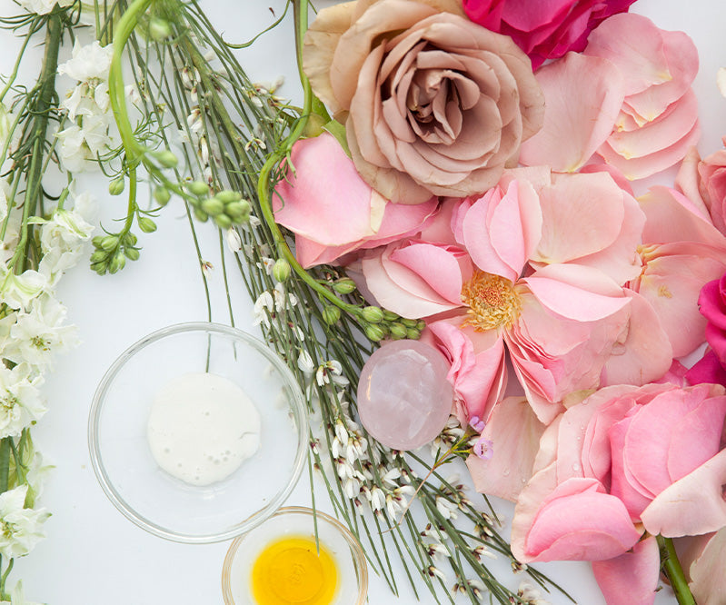 Pink roses, white flowers, and skincare ingredients in glass bowls on white background