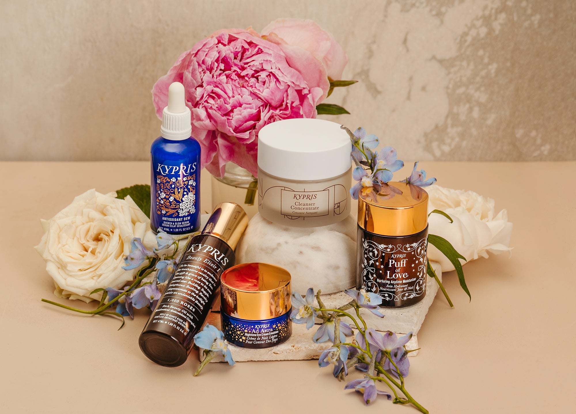 KYPRIS skincare products with flowers: Antioxidant Dew, Cleanser Concentrate, Puff of Love, Beauty Elixir, Ad Astra
