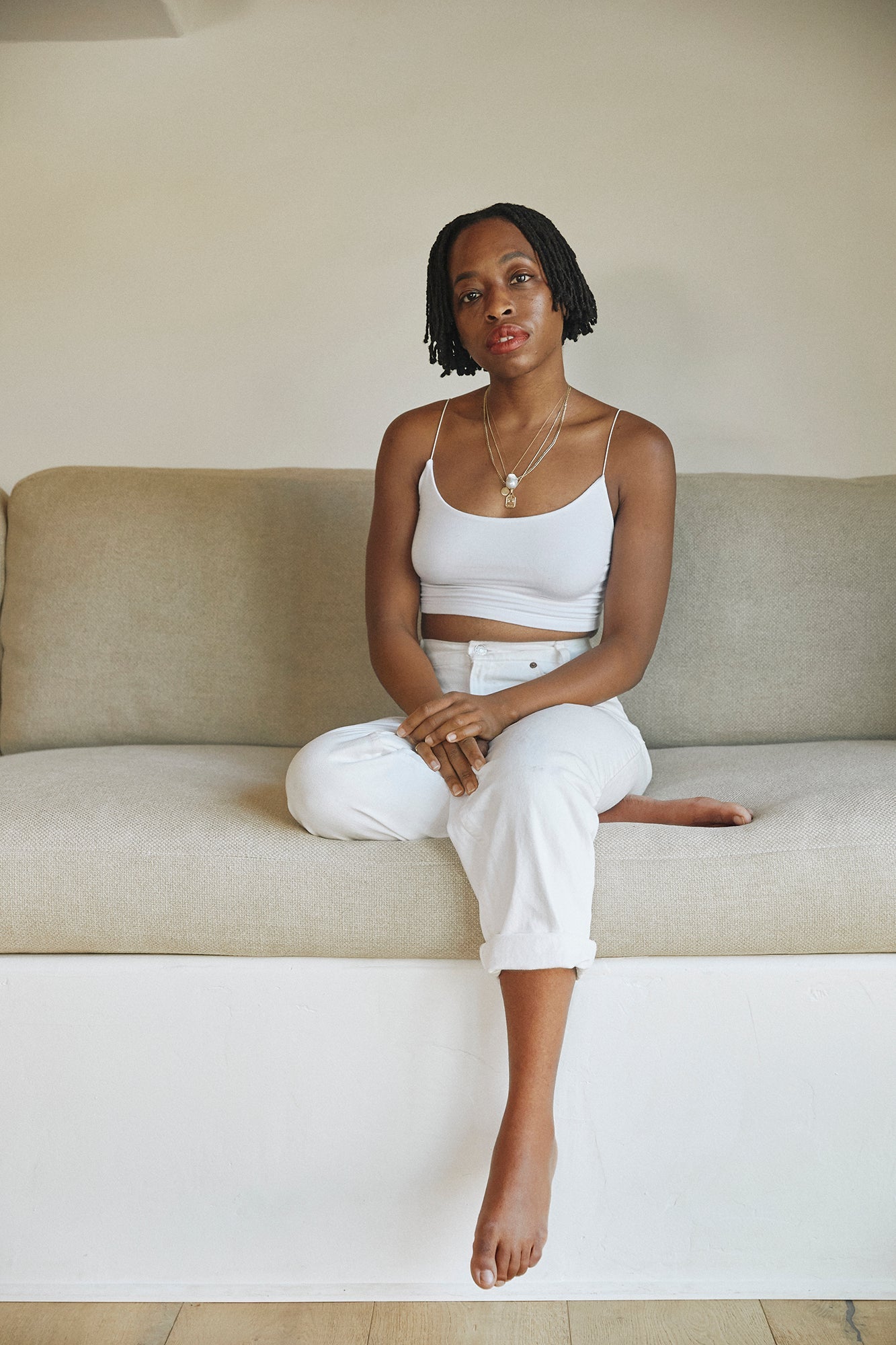 Woman in white crop top and pants sitting on beige couch