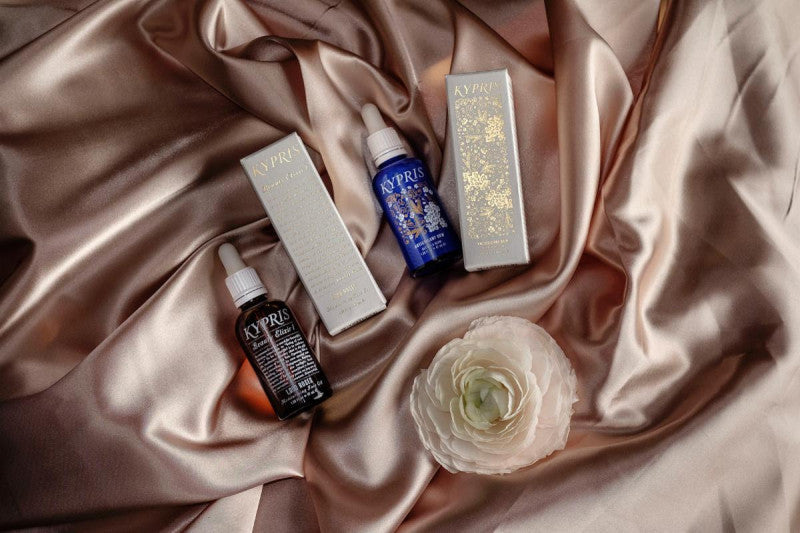KYPRIS Beauty Elixir serums & boxes on satin with white flower, organic skincare