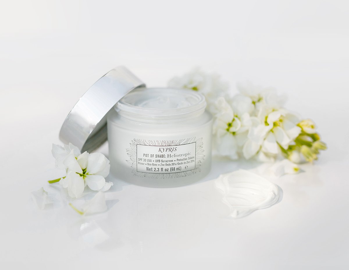 Pot of Shade: Heliotropic SPF 30, in frosted glass jar with white lid, surrounded by flowers.