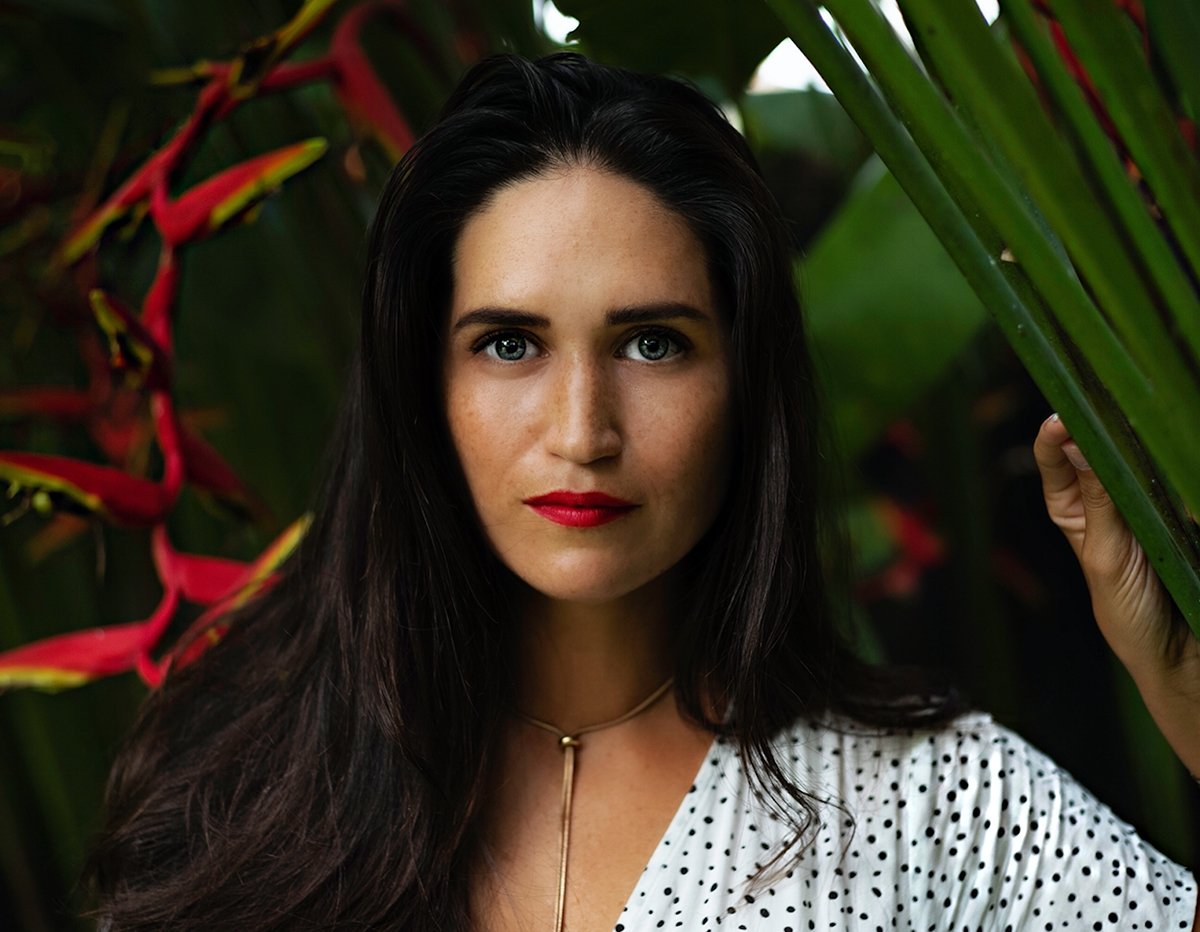 Woman with red lipstick and polka dot blouse amidst tropical greenery