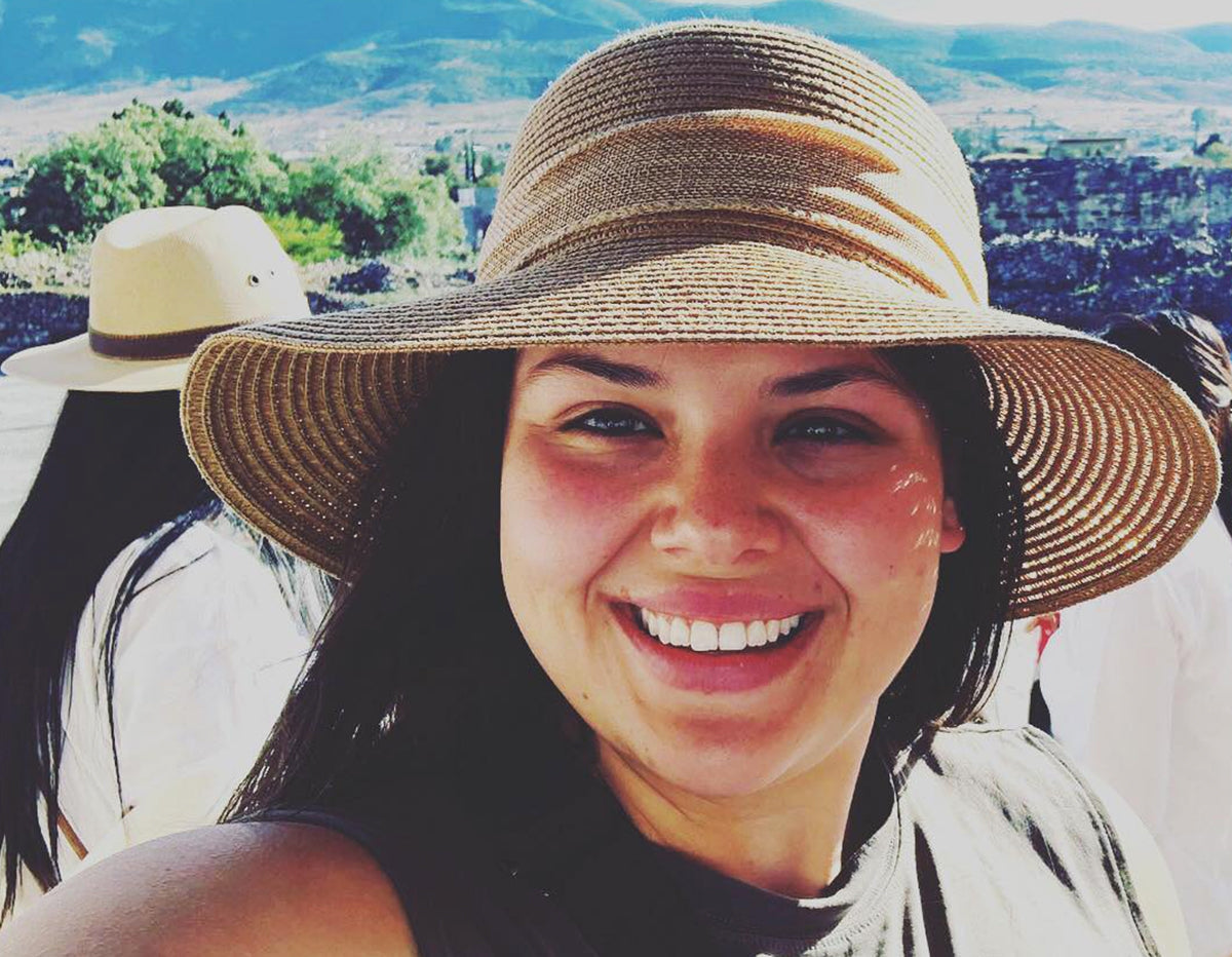 Smiling woman wearing a wide-brimmed straw hat outdoors with scenic hills background