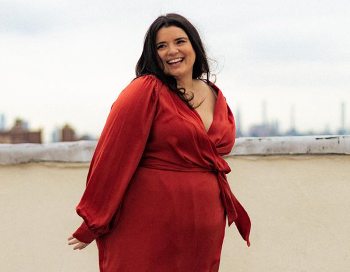 Woman in red wrap dress smiling on rooftop with city skyline background