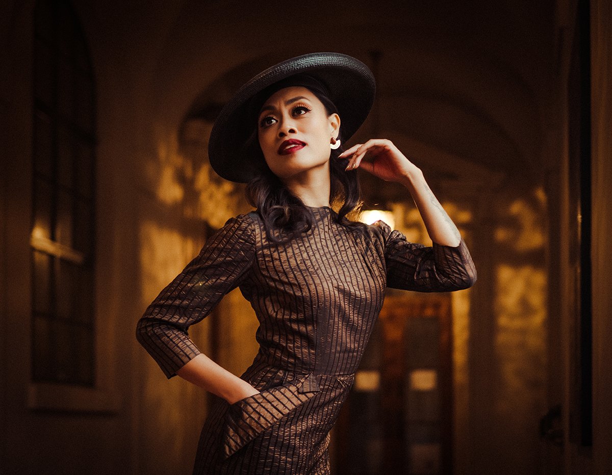 Elegant woman in striped dress and black hat posing in warm-lit hallway