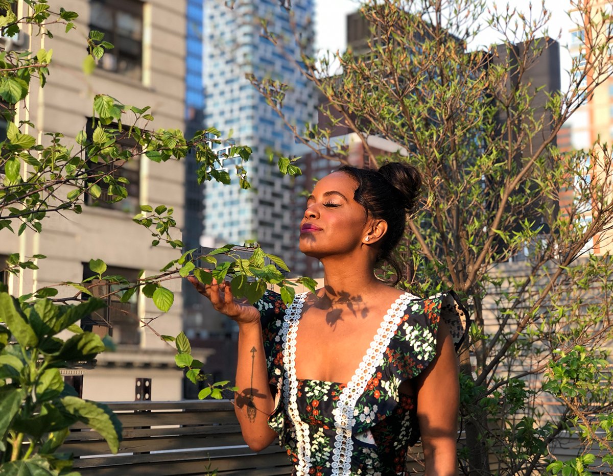 Woman in floral dress enjoying fresh green leaves on rooftop garden with city skyline background