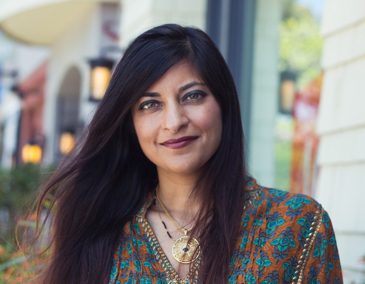Woman with long dark hair wearing patterned top and gold necklace outdoors