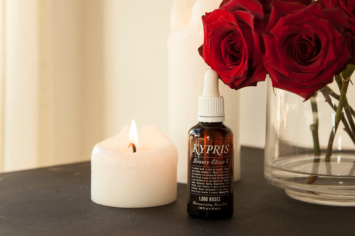 Beauty Elixir I: 1,000 Roses in amber glass bottle, next to a candle and red roses.