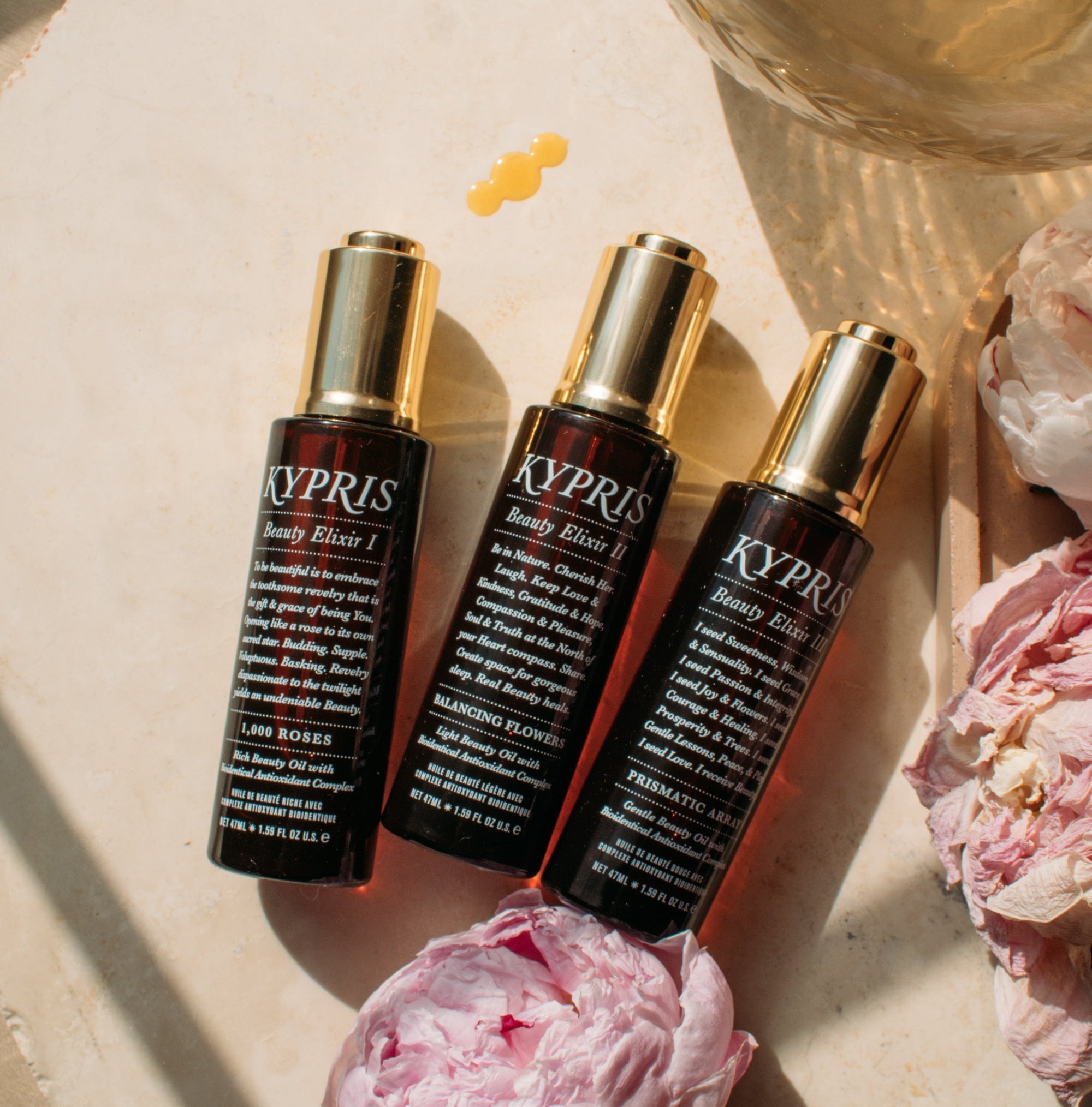 KYPRIS Beauty Elixir I, II, III bottles with pink peonies and golden droplet on marble