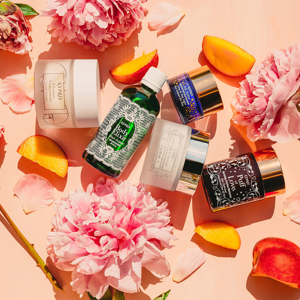KYPRIS Body Elixir, Puff of Love, and other skincare products with pink peonies and peach slices