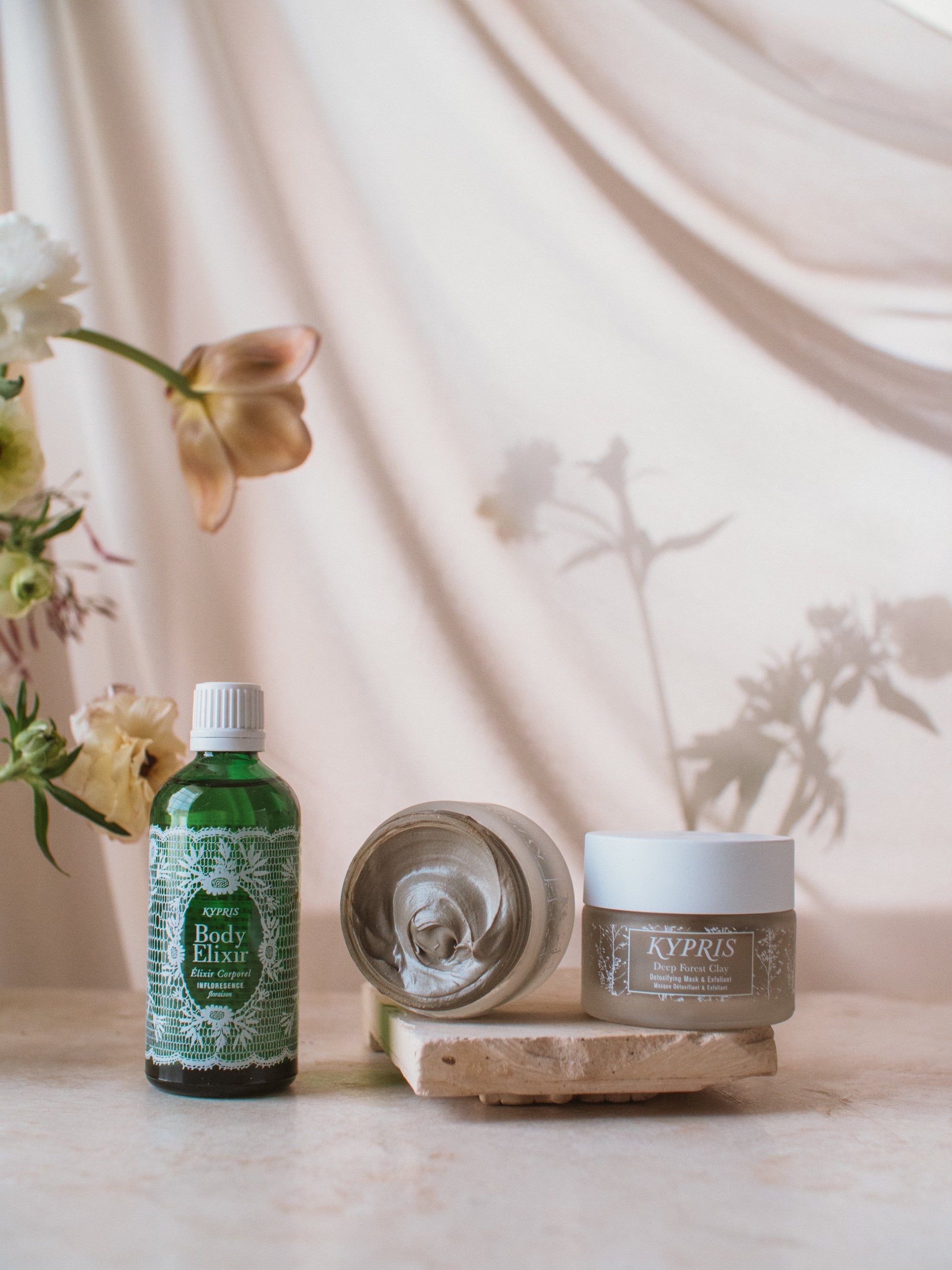 KYPRIS Body Elixir and Deep Forest Clay Detoxifying Mask with floral backdrop