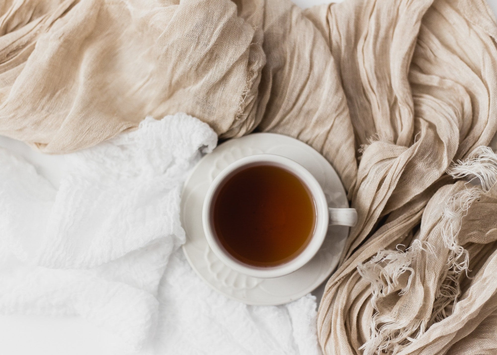 Cup of tea on white saucer with beige and white textured fabrics
