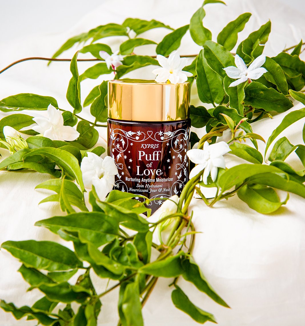 Puff of Love Moisturizer, in amber glass jar with gold lid, in a bed of jasmine. 
