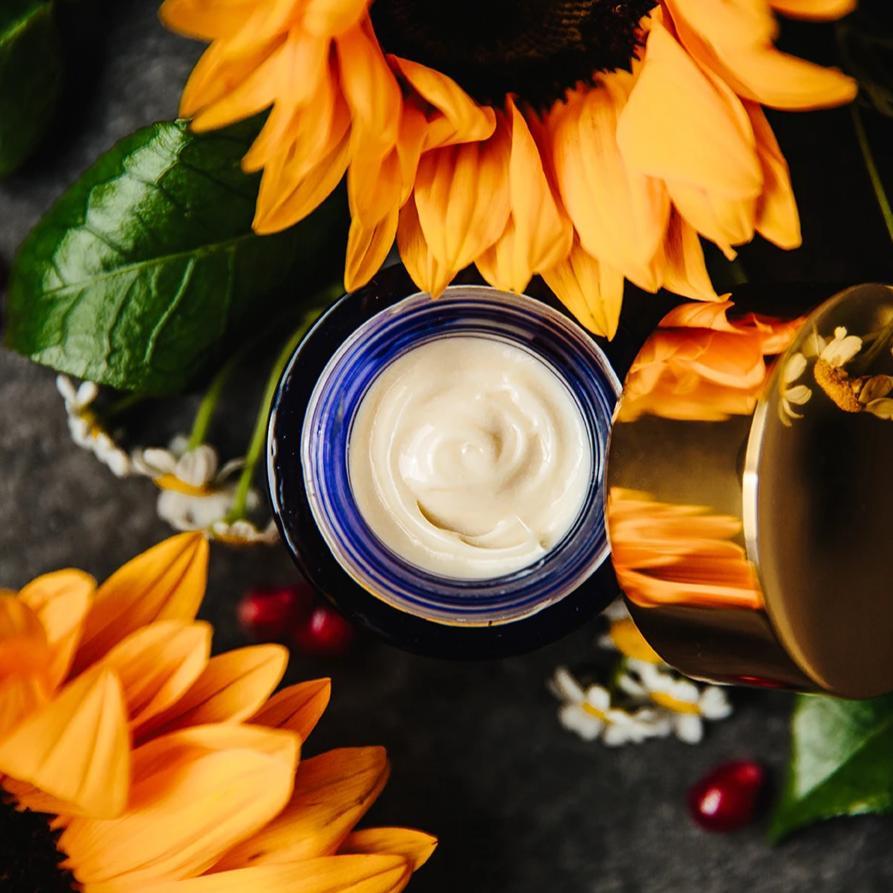 Ad Astra Nighttime Eye Cream emulsion, open, showing creamy white texture, on a bed of sunflowers. 