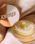 Lip Balm Elixir, in frosted jar with gold lid, on textured surface.