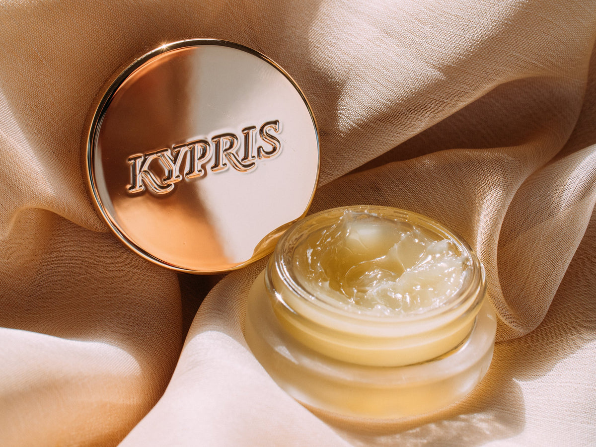 Lip Balm Elixir, in frosted jar with gold lid, on textured surface.